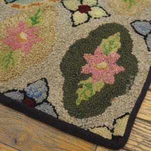 Corner of a multicolored hooked rug featuring pink and green florals on a mottled beige field over wood planks.