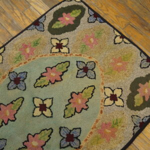 Hooked rug featuring colorful floral designs on beige and teal fields, displayed on hardwood planks.