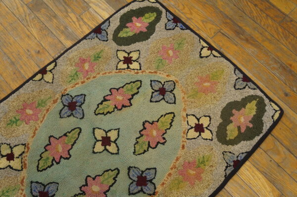 Hooked rug featuring colorful floral designs on beige and teal fields, displayed on hardwood planks.