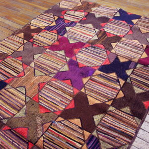A multicolored geometric rug displaying alternating striped diamond and solid star shapes rests on worn wooden flooring.