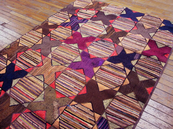 A multicolored geometric rug displaying alternating striped diamond and solid star shapes rests on worn wooden flooring.