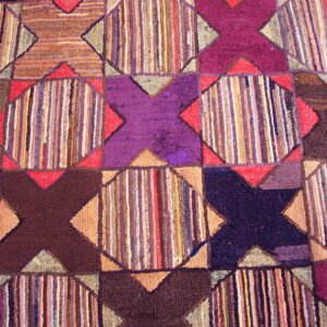 Varied texture rug with geometric purple and brown X-shapes framing sections of colorful vertical stripes.