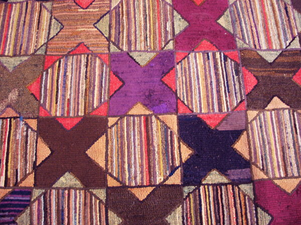 Varied texture rug with geometric purple and brown x-shapes framing sections of colorful vertical stripes.