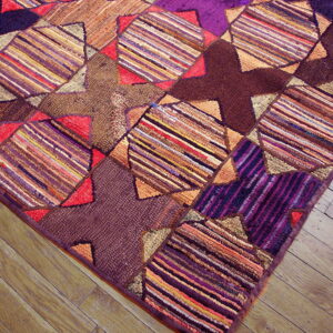 Multicolored patchwork rug with textured stripes and dark geometric patterns rests on light hardwood flooring.