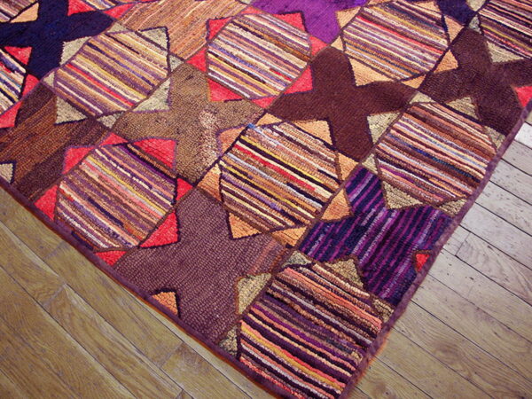 Multicolored patchwork rug with textured stripes and dark geometric patterns rests on light hardwood flooring.