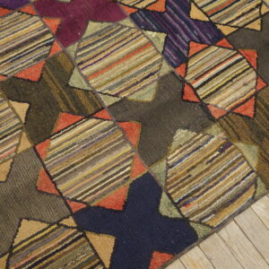 A multicolored hooked rug with a geometric patchwork pattern sits on light, weathered wood flooring.