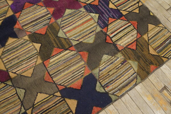 A multicolored hooked rug with a geometric patchwork pattern sits on light, weathered wood flooring.