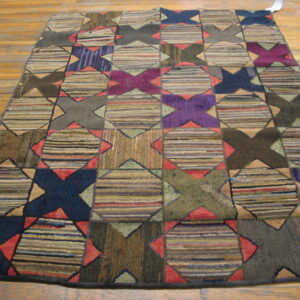 Textured, multi-color rug with repeating geometric star and striped block patterns on wood plank flooring.