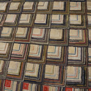 Textured rug featuring a repeating log cabin quilt pattern in beige, red, dark blue, and brown tones.