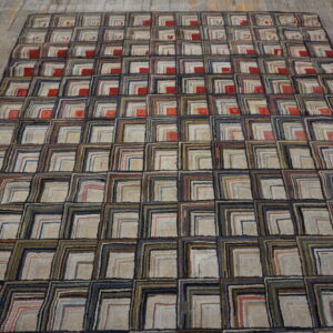 Textured rug featuring repeating multicolor squares with beige centers and navy borders on distressed wood planks.