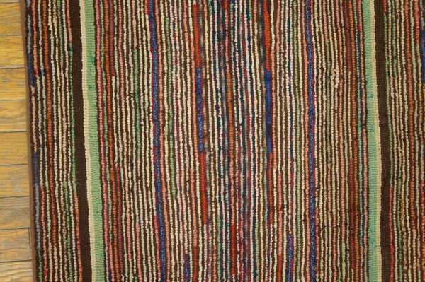 Textured rug with dense vertical stripes in brown, green, cream, red, and blue on wood flooring.
