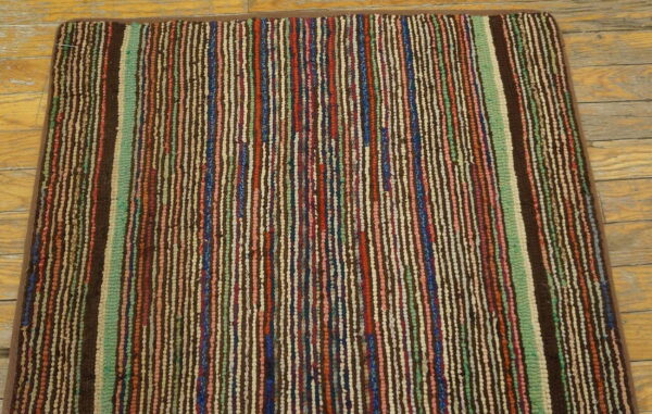 Textured rug with thin vertical stripes of brown, red, green, blue, and cream on light wood planks.