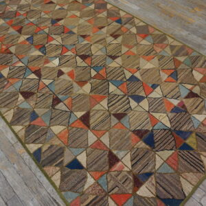 A textured rug with a brown geometric patchwork of colorful triangles lies on distressed gray wood planks.