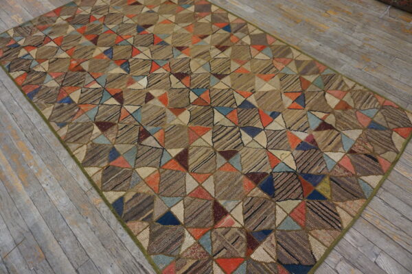 A textured rug with a brown geometric patchwork of colorful triangles lies on distressed gray wood planks.