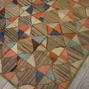 Multi-colored geometric patchwork rug with visible texture, laid upon weathered gray wooden floorboards.