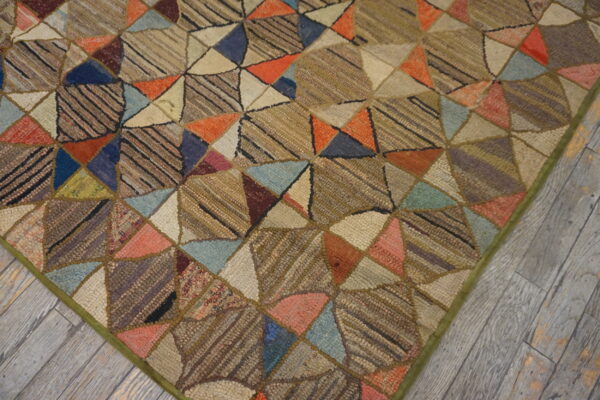 Multi-colored geometric patchwork rug with visible texture, laid upon weathered gray wooden floorboards.