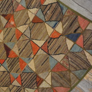 Low-pile geometric patchwork rug in brown, orange, blue, and cream on distressed wood floor.