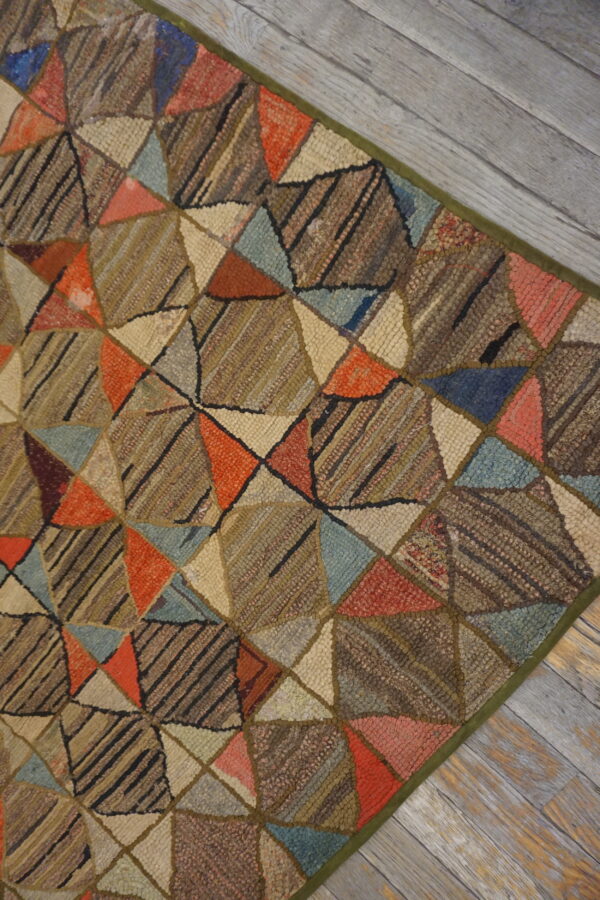 Low-pile geometric patchwork rug in brown, orange, blue, and cream on distressed wood floor.