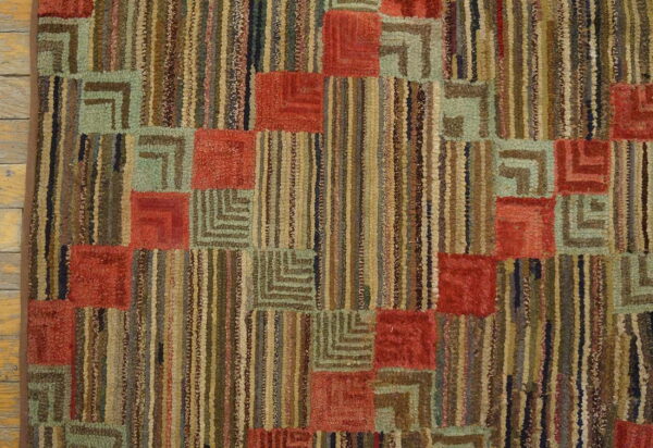 Geometric rug with rust red squares, l-shaped sage patterns, and vertical multicolor stripes on wood floor.