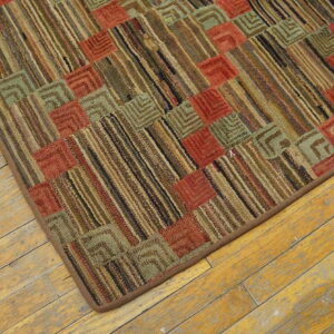 Rustic, low-pile rug with a geometric grid of red, sage, and brown stripes on worn wood flooring.