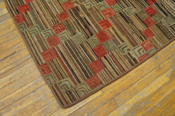 Rustic, low-pile rug with a geometric grid of red, sage, and brown stripes on worn wood flooring.