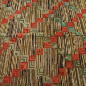 Textured rug with multicolored stripes and geometric squares in coral and teal green on wood floor.