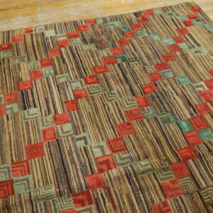 Highly textured rug with vertical striped earth tones and repeating red and teal geometric blocks on wood planks.