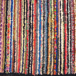 Highly textured rag rug composed of vertical multicolored fabric strips and a dark outer edge.