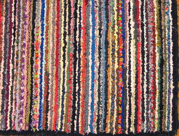 Highly textured rag rug composed of vertical multicolored fabric strips and a dark outer edge.