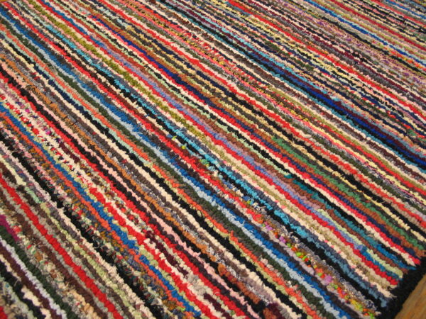 A brightly multicolored braided rag rug features narrow parallel strips of red, blue, green, and black fibers.