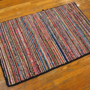 Textured rag rug with thin, multicolored vertical stripes displayed on warm-toned hardwood flooring.
