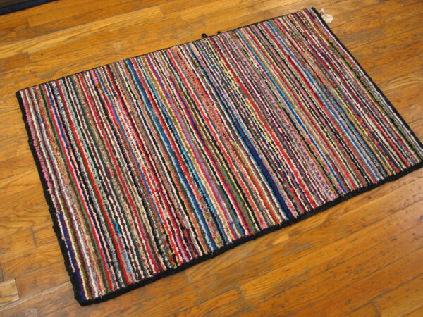Textured rag rug with thin, multicolored vertical stripes displayed on warm-toned hardwood flooring.