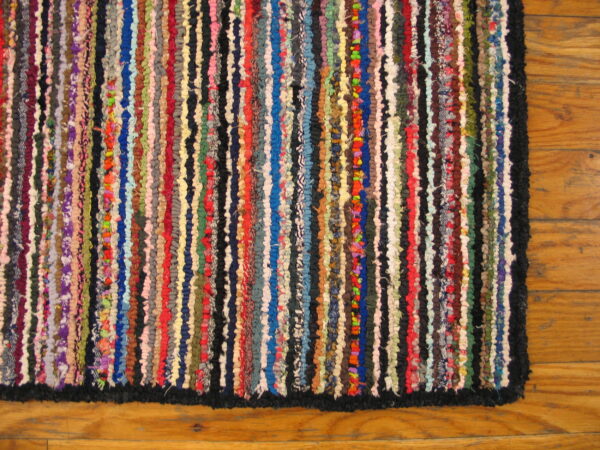Highly textured multicolor rag rug with vertical stripes rests on wood plank flooring.