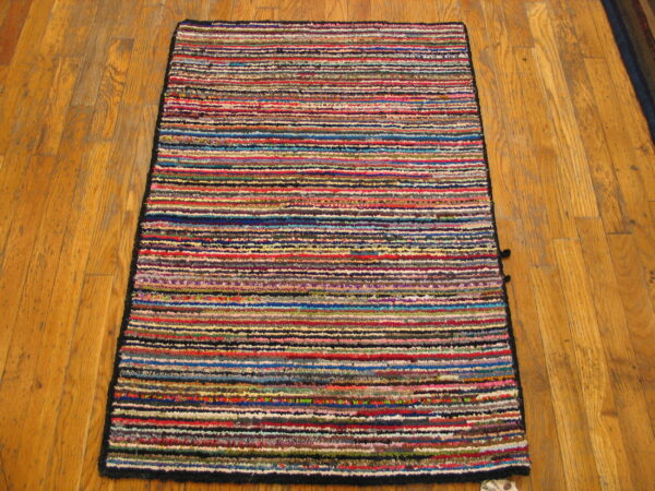 A textured rag rug with dense, multicolored horizontal stripes sits on natural hardwood flooring.