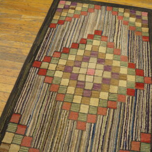 Textured rug featuring a colorful checkered diamond pattern on a striped field, set on wood plank flooring.