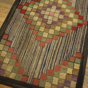 Multicolored textured rug with central squares and vertical stripes in rust, purple, and green on wood flooring.