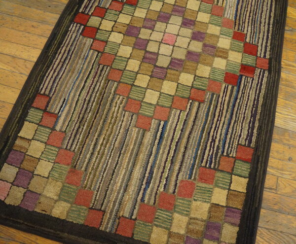 Multicolored textured rug with central squares and vertical stripes in rust, purple, and green on wood flooring.