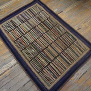 Rectangular rug with multicolored stripes partitioned into a grid, framed by a dark blue border on wood flooring.