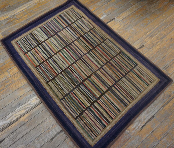 Rectangular rug with multicolored stripes partitioned into a grid, framed by a dark blue border on wood flooring.