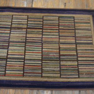 Multi-colored striped rug with a dark blue border rests on rustic, worn light brown wood flooring.