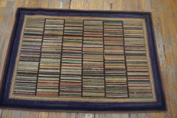 Multi-colored striped rug with a dark blue border rests on rustic, worn light brown wood flooring.