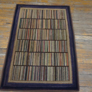 Low-pile rug with vertical multicolored stripes and a dark blue border rests on distressed hardwood floor.