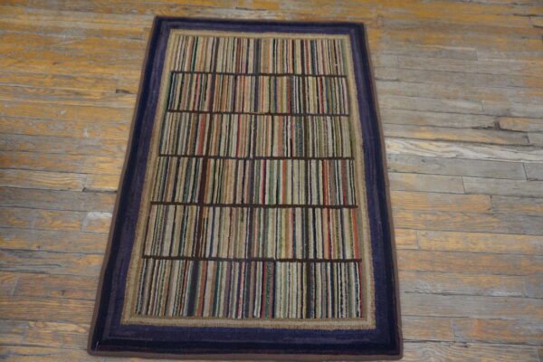 Low-pile rug with vertical multicolored stripes and a dark blue border rests on distressed hardwood floor.