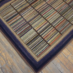 Multicolor striped rug with a dark grid and indigo border detail sits on light, rustic wood planks.
