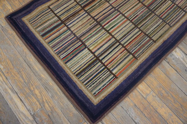 Multicolor striped rug with a dark grid and indigo border detail sits on light, rustic wood planks.