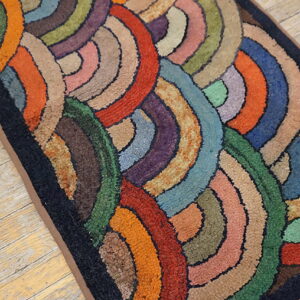 Multicolored hooked rug runner featuring chunky concentric arcs rests on light wood planks.