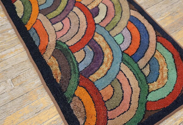 Multicolored hooked rug runner featuring chunky concentric arcs rests on light wood planks.