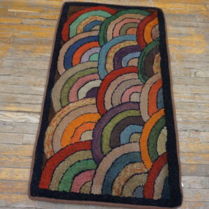 A rectangular rug with textured, multi-colored overlapping arcs lies on distressed wooden flooring.