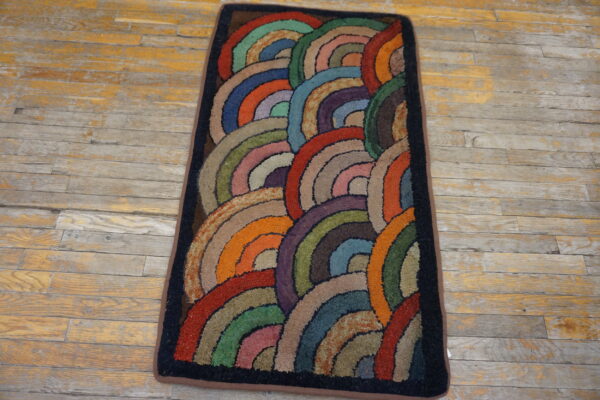 A rectangular rug with textured, multi-colored overlapping arcs lies on distressed wooden flooring.