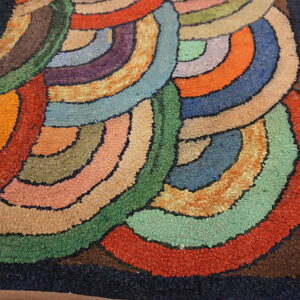 Shaggy, textured rug displaying an abstract pattern of colorful concentric arcs on light wooden floorboards.